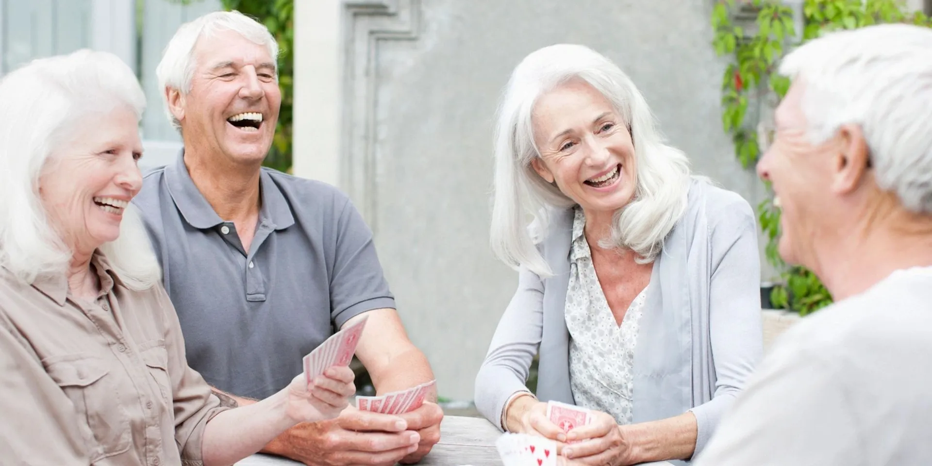 Quatre aînés souriants jouent aux cartes autour d'une table, à l'extérieur
